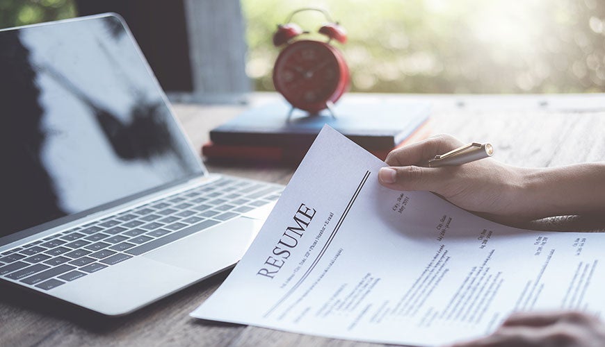 a person holds a printed resume in front of their laptop