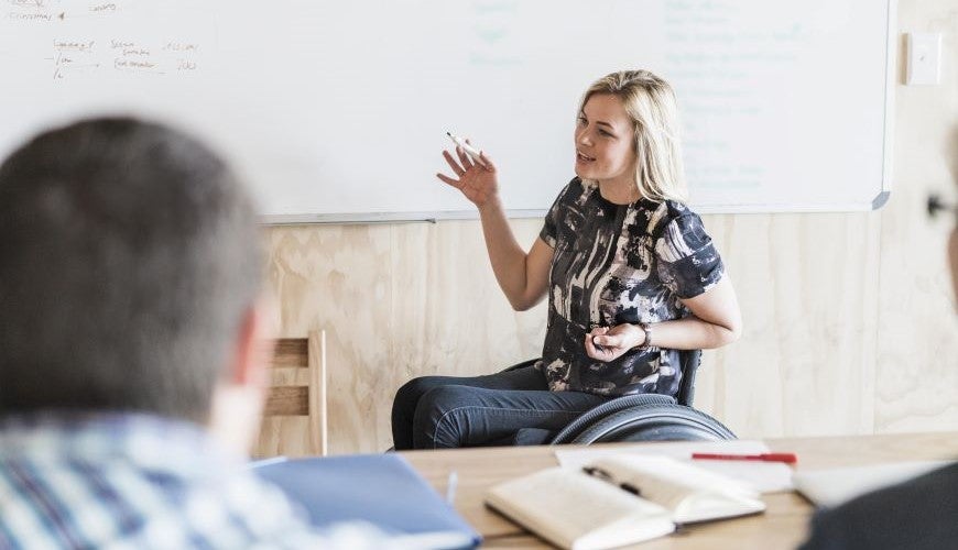 A pesron sits in a wheelchair giving a presentation at a whiteboard