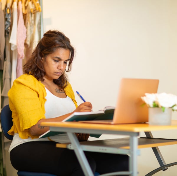 Lady sitting in front of computer writing in book