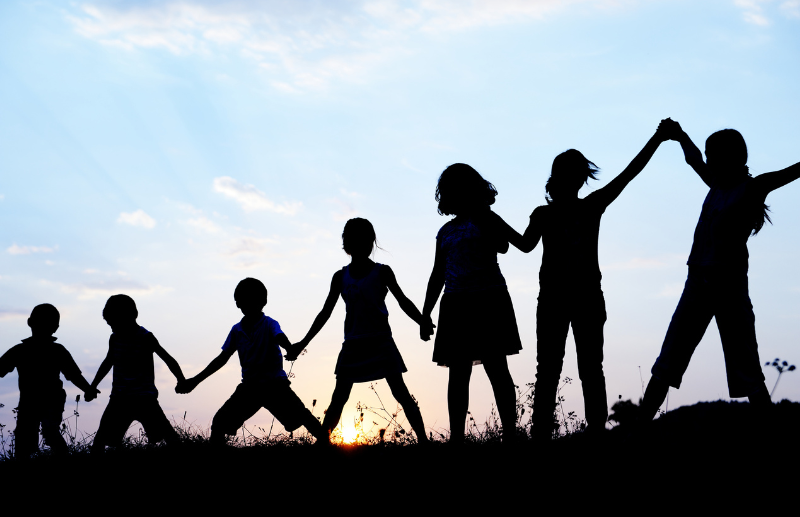 children holding hands on a hill at sunset