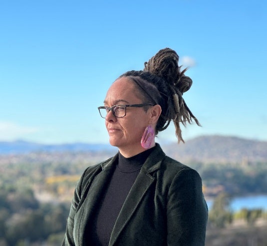 Woman in dark green blazer with glasses and pink earrings