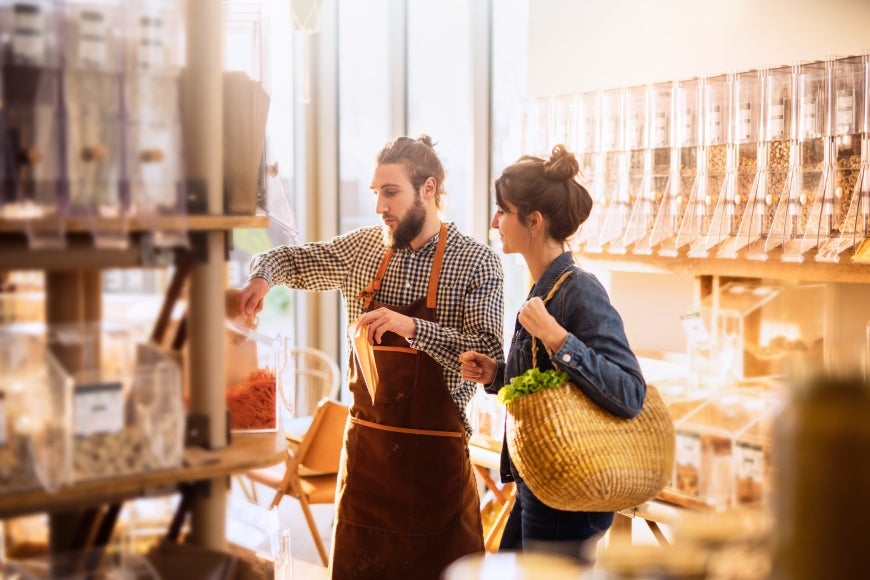 A wide shot of a supermarket store worker assisting a customer with purchasing herbs.