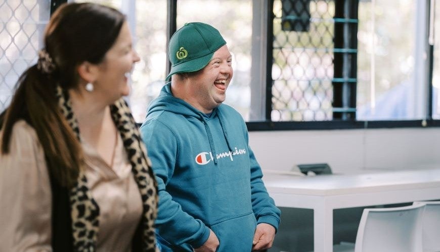 Two people side on smiling and laughing. The man is wearing a Woolworths hat. 