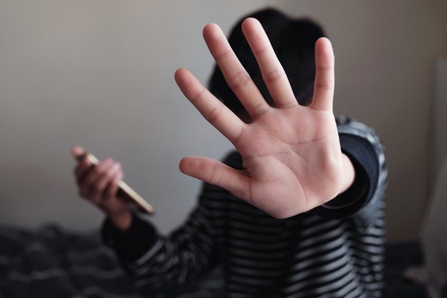 Teenage Asian boy holding a smartphone and showing a stop sign with his hand.