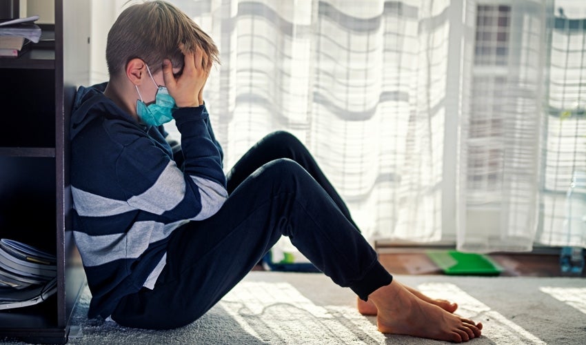 Child wearing a facemask sitting with head in hands