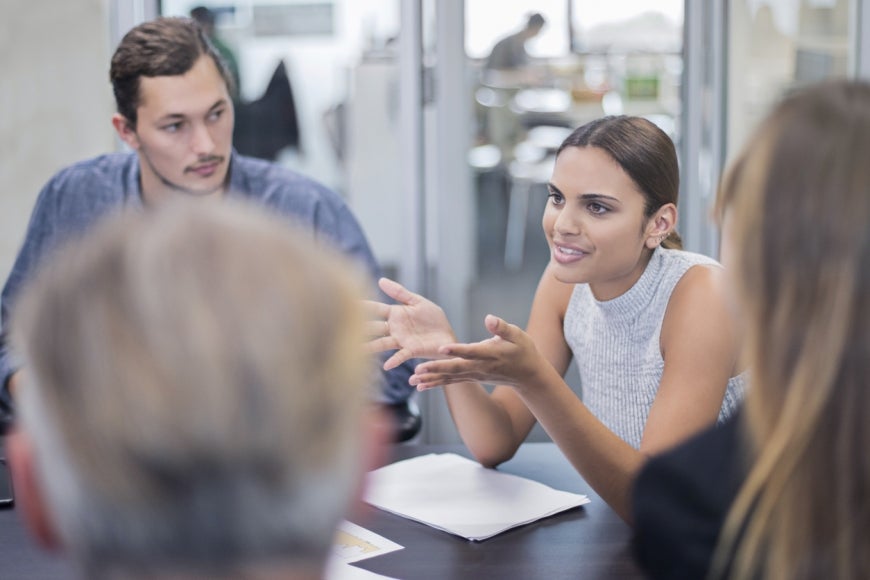 A young woman and man at work among a group of people sitting an office.