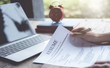 a person holds a printed resume in front of their laptop