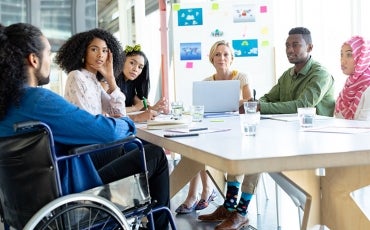 People sitting at a boardroom table, one of who is in a wheelchair