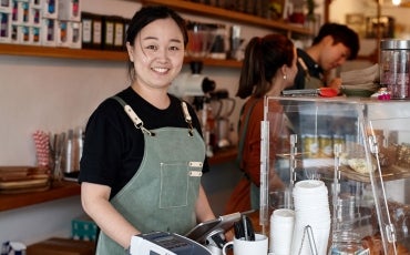 Shop owner smiling whilst working inside coffee shop.