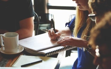 A group of people sitting around a wooden table contributing to writing a report