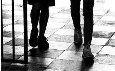 Black and white image showing the legs of a schoolboy and girl as they walk on chequered tiles.