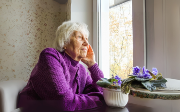 older woman in purple jumper look out a window