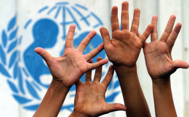 children's hands raised in front of united nations logo