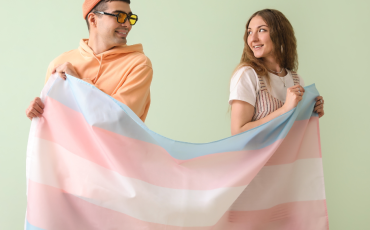 2 young poepl standing behind a trans flag