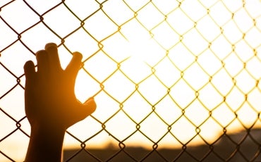 Young hand holds fence as sun sets in distance