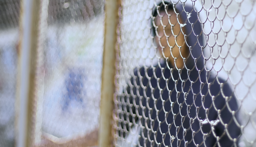 Boy wearing hoodie behind a wire fence