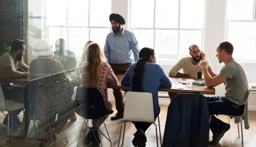 Racially diverse group of 9 men and women chatting collaboratively around a table.