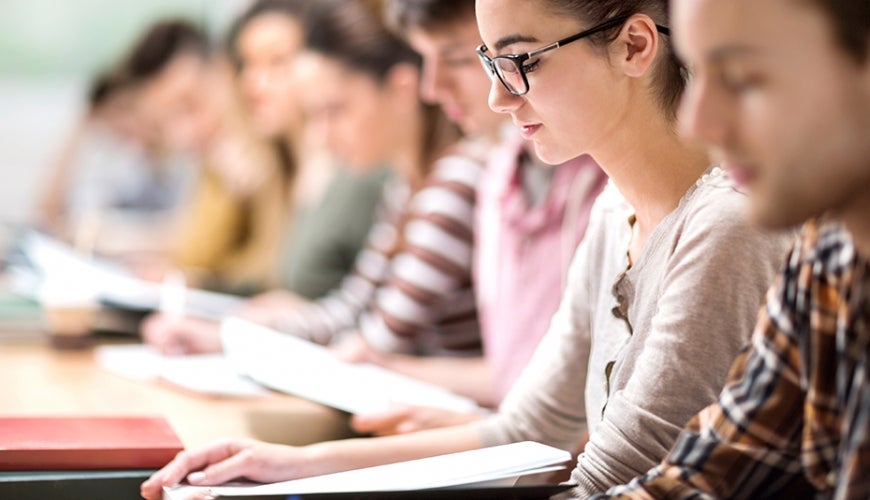 College students sitting in a classroom reading a booklet.