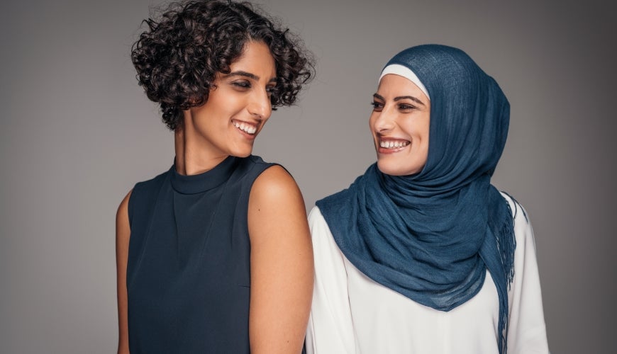 "Portrait of two beautiful smiling women of Middle Eastern heritage, one wearing hijab.""