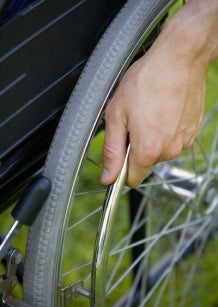 A close-up view of one wheel of wheelchair. A person is holding the wheel. 