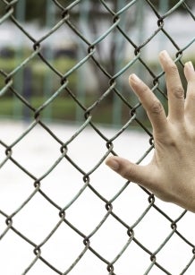 A woman's hand holds onto the fencing of a detention facility