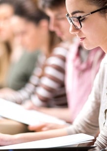 College students sitting in a classroom reading a booklet.