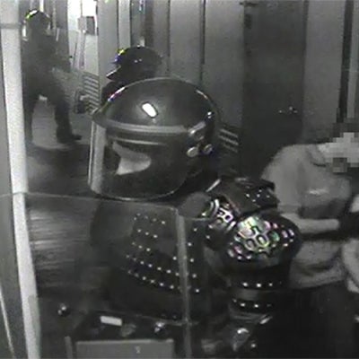 still from incident video: guard in body armour on alert and another guard leads child away