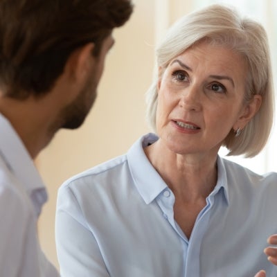 Older professional woman with fair hair talking to a young man.