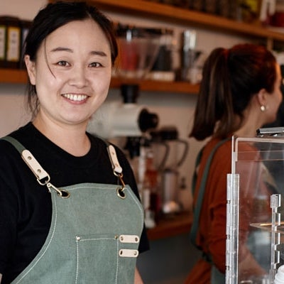 Shop owner smiling whilst working inside coffee shop.