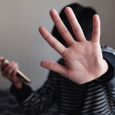 Teenage Asian boy holding a smartphone and showing a stop sign with his hand.