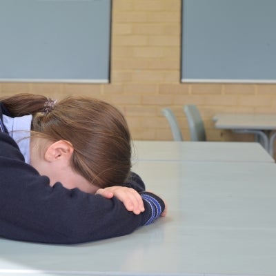 School girl sitting at desk with head in hands.