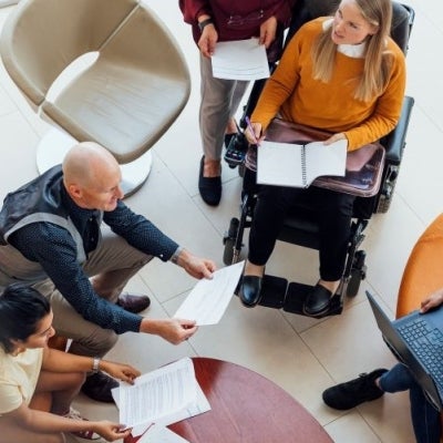 Group of people sitting around a table holding paper and laptops and discussing something 