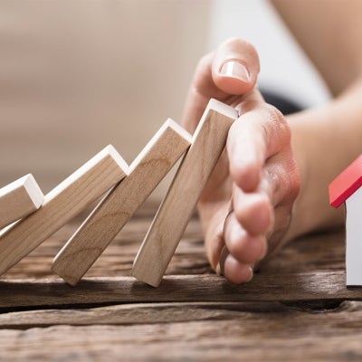 female hand catching blocks about to topple onto toy house