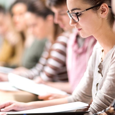 College students sitting in a classroom reading a booklet.